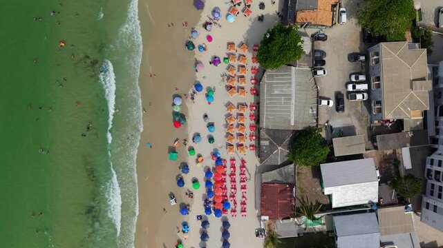 Praia dos Ingleses in Florian&oacute;polis Santa Catarina Brazil on Atlantic Ocean with dense umbrella patterns and shoreline waves in Mata Atl&acirc;ntica coastal setting, drone top down vertical shot