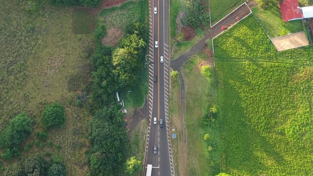 BR 277 in Laranjeiras do Sul Paran&aacute; Brazil with highway lanes, vehicles, and surrounding agricultural land in rural landscape near toll station, drone top down panning shot