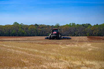 Fototapeta premium Tractor operates on plowed field soil. Tractor supports heavy tillage with disc. Farm machinery uses tractor for cultivation. Blue sky frames tractor in landscape.