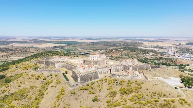 Drone shot of the historic Forte de Nossa Senhora da Graca near Elvas, Portugal, surrounded by rolling hills and countryside under a clear blue sky.
