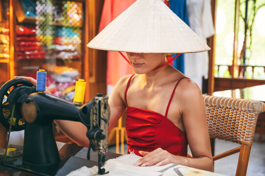 A Vietnamese seamstress in a conical hat reshapes and repairs clothes in a traditional atelier