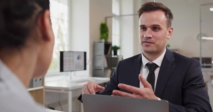 Advisor and client meeting for office consultation. Manager reviews contract terms on laptop, checking document notes at the office desk. Professional business advisory and service concept.