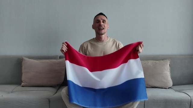 A Dutch football fan watches football and supports his favorite team while holding the Dutch flag