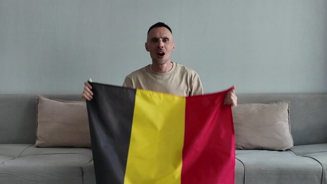 A Belgian football fan watches football and supports his favorite team while holding the Belgian flag