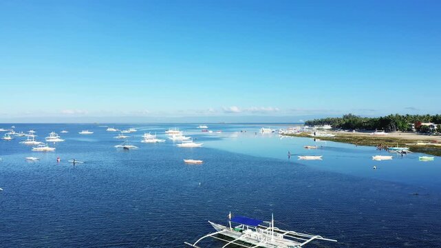 Scenic view of traditional outrigger boats floating on calm blue waters near the coastline of Bohol island, Philippines, under a clear sky.