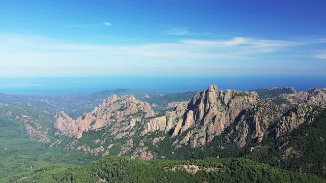 Wide panoramic view of the rugged Col de Bavella mountains in Corsica, with dramatic rocky peaks and lush green forest under a clear blue sky.