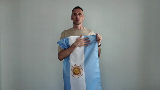 A patriotic man proudly sings the Argentine national anthem while holding the Argentine flag. An emotional sports fan cheers on his favorite team