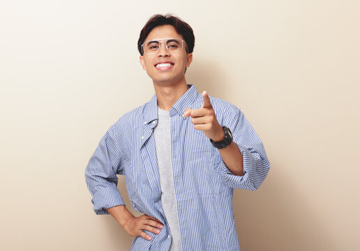 Smiling confident young Asian man pointing finger at camera on isolated background.