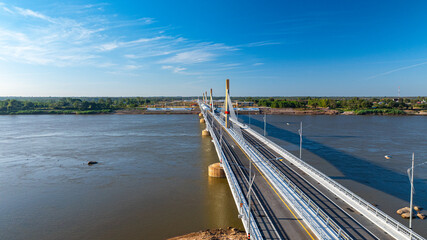 Fototapeta premium A breathtaking aerial view of a modern bridge crossing the Mekong River, symbolizing international connectivity between Thailand and Laos under a clear blue sky.