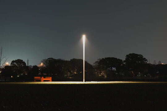 A lonely street lamp casting a solitary pool of light in a nearly jet-black public park at night.