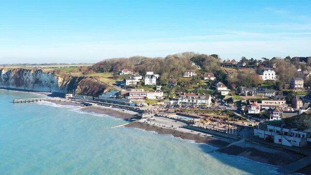 Scenic aerial view of Veules les Roses with pebble beach, seaside promenade, and dramatic cliffs under a clear blue sky in Normandy, France.