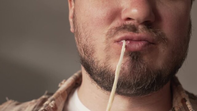 A man takes a close-up bite of a cooked sandwich, from which the melted cheese stretches.