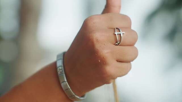 Closeup hands releasing beach sand slowly, silver bracelet and ring, palm trees bokeh, soft sunset glow, grains falling between fingers, meditative seaside atmosphere, tactile texture emphasized,