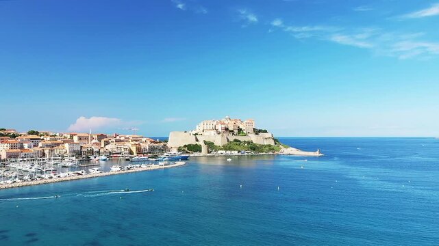 Scenic view of Calvi citadel overlooking a vibrant marina and the clear blue Mediterranean Sea under a sunny sky in Corsica, France.