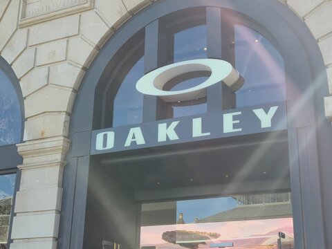 London UK 04.07.2025 Oakley retail storefront with iconic logo above modern entrance featuring large arched window and sun flare highlighting sporty eyewear brand identity in urban shopping district