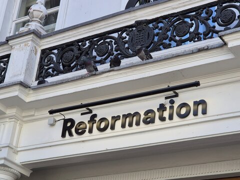 London UK 04.07.2025 Reformation fashion store sign on elegant white building facade with decorative balcony and pigeons reflecting sustainable clothing brand presence in london shopping area