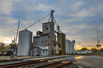 Obraz premium Grain elevators and railroad tracks at sunset in small town