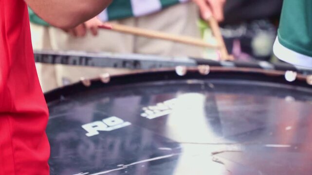 Drummer playing a big drum with sticks. Dynamic close-up of percussion performance in a lively outdoor setting.