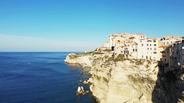 Scenic view of Bonifacio s historic buildings perched on dramatic limestone cliffs above the blue Mediterranean Sea in Corsica, France. Bright sunlight highlights the coastal landscape and