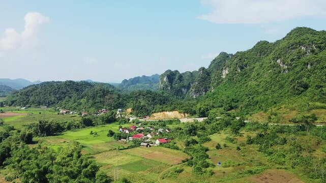 Aerial view of a small village surrounded by green fields and forested mountains along the Lang Son to Cao Bang route in northern Vietnam. Bright, sunny day with clear skies and vibrant natural
