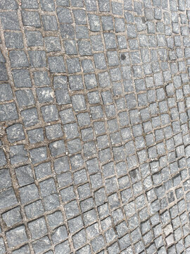 Close-up of square cobblestone pavement with structured stone blocks forming a repeating surface pattern.