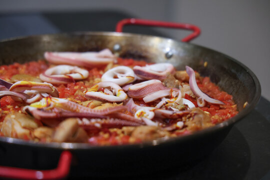 Spanish Paella Cooking in Large Pan with Squid and Tomato Sauce