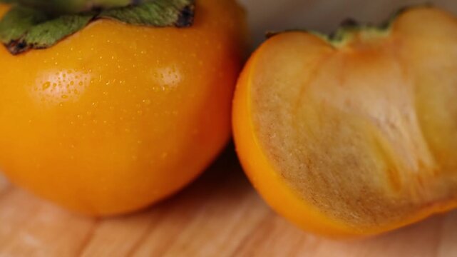 Juicy persimmon fruit sliced in half showing texture and water droplets on wooden board.