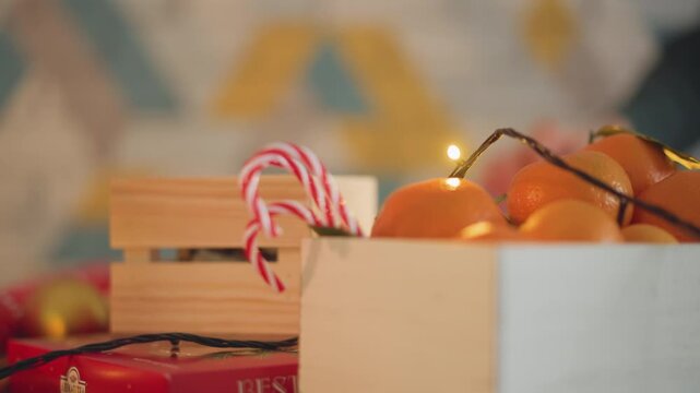 Crate oranges candy canes christmas lights, wooden box filled tangerines and striped candy canes, warm fairy lights creating soft bokeh, red wrapping paper peeking underneath, cozy rustic holiday