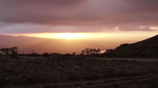 Serra da Boneca in Penafiel Porto District Norte Portugal with rocky ridge, sparse vegetation, and human silhouette overlooking Douro Valley under sunset sky, drone pullback