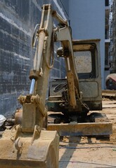 Fototapeta premium A construction excavator parked on a construction site. The machine is covered in dirt and grime, indicating recent use. The background features a partially constructed building.
