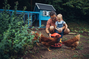 Father and toddler feeding chickens in backyard garden. © Halfpoint