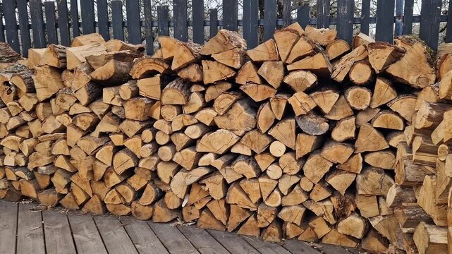 Wooden logs stacked in a pile near the fence. Firewood ready for use. Stacked wooden logs. Close-up of stacked firewood. Natural wooden background. Ecological heating concept