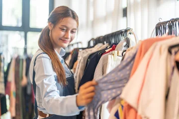 Happy female small business owner in denim apron checking clothing rack in fashion boutique, Retail store manager arranging apparel inventory, SME entrepreneur lifestyle and shop management concept © Art_Photo