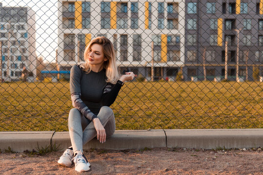 Woman in athletic wear sitting by a fence with modern buildings in the background