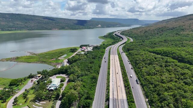 Aerial view of highway running along river and green hills. Transportation, infrastructure, travel and logistics concept