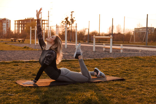 Woman practicing yoga cobra pose on mat outdoors at sunset