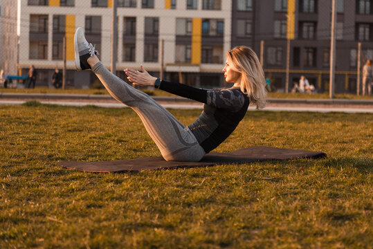 Woman performing boat pose on yoga mat outdoors during golden hour