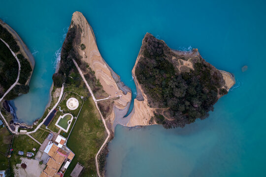 Aerial view of Canal d'Amour in Sidari, Corfu, Greece, showcasing unique sandstone rock formations and turquoise Ionian Sea at sunset with coastal town.