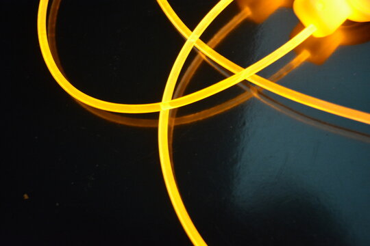 Light guides wire, cable, polyethylene tubes, rods with beautiful orange, yellow light are located on a black glossy background with small reflections from the wires in complete darkness.
