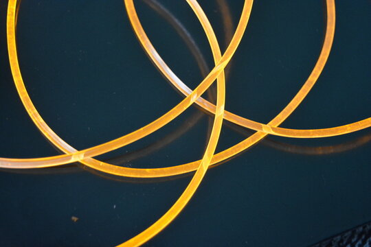 Light guides wire, cable, polyethylene tubes, rods with beautiful orange, yellow light are located on a black glossy background with small reflections from the wires in complete darkness.