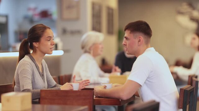 Girl in cafe sits near guy companion and drink coffee, has nice conversation and discuss news of day. Cozy atmosphere of cafe, meeting place for friend, business partner, relative
