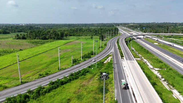Aerial view of modern highway interchange with multilayer roads and curved ramps surrounded by green farmland, showcasing transportation infrastructure, urban development, and road network planning.