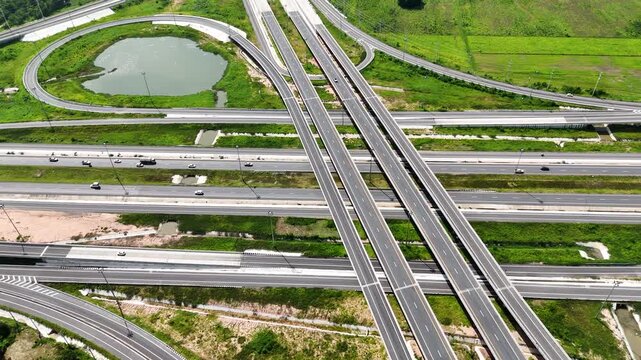 Aerial view of modern highway interchange with multilayer roads and curved ramps surrounded by green farmland, showcasing transportation infrastructure, urban development, and road network planning.