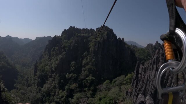 POV ziplining shot down a huge zipline between karst limestone formations and jagged mountain peaks in southern Laos.