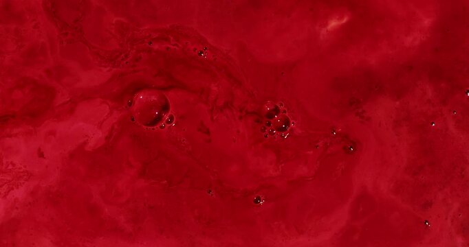 Slow moving red liquid with large, medium and small bubbles.