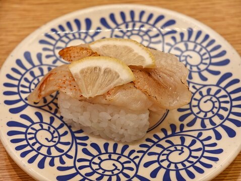 Aburi fish nigiri sushi topped with lemon slices on patterned plate