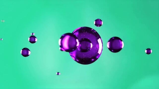 A minimalist 3D animation of shiny, viscous purple liquid drops or spheres floating weightlessly against a teal green background. Ideal for cosmetics, pharmaceuticals, or high-tech material design con