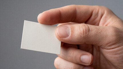 Fototapeta premium Hand holds a blank card in a neutral setting during daylight hours