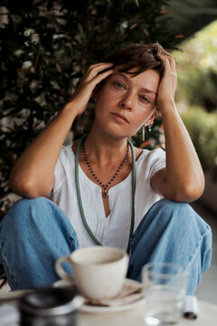 Worried woman holding head in hands sitting outdoors next to coffee