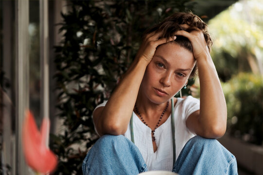 Stressed young woman sitting outdoors with hands holding head